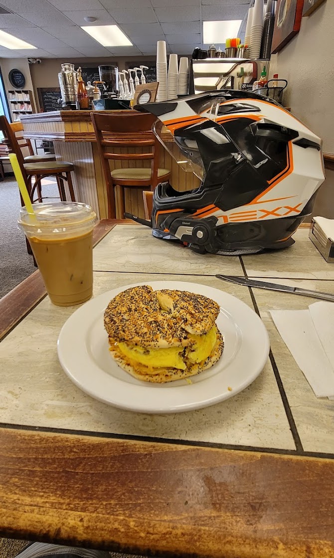 Everything bagel breakfast sandwich with egg and an iced coffee beside a motorcycle helmet